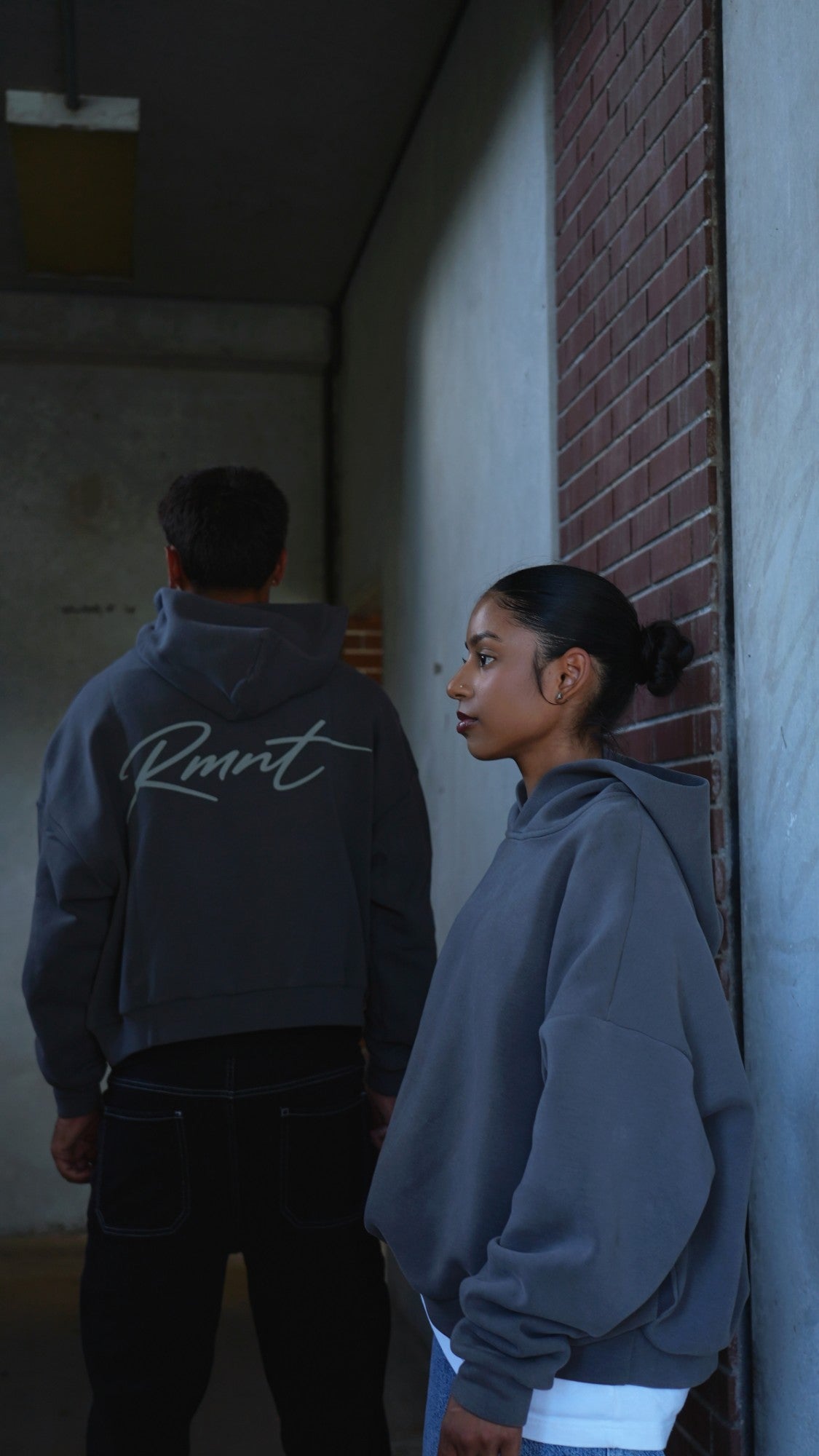Two people wearing the Slate Grey RMNT Signature Hoodie, one showing the Rmnt script on the back